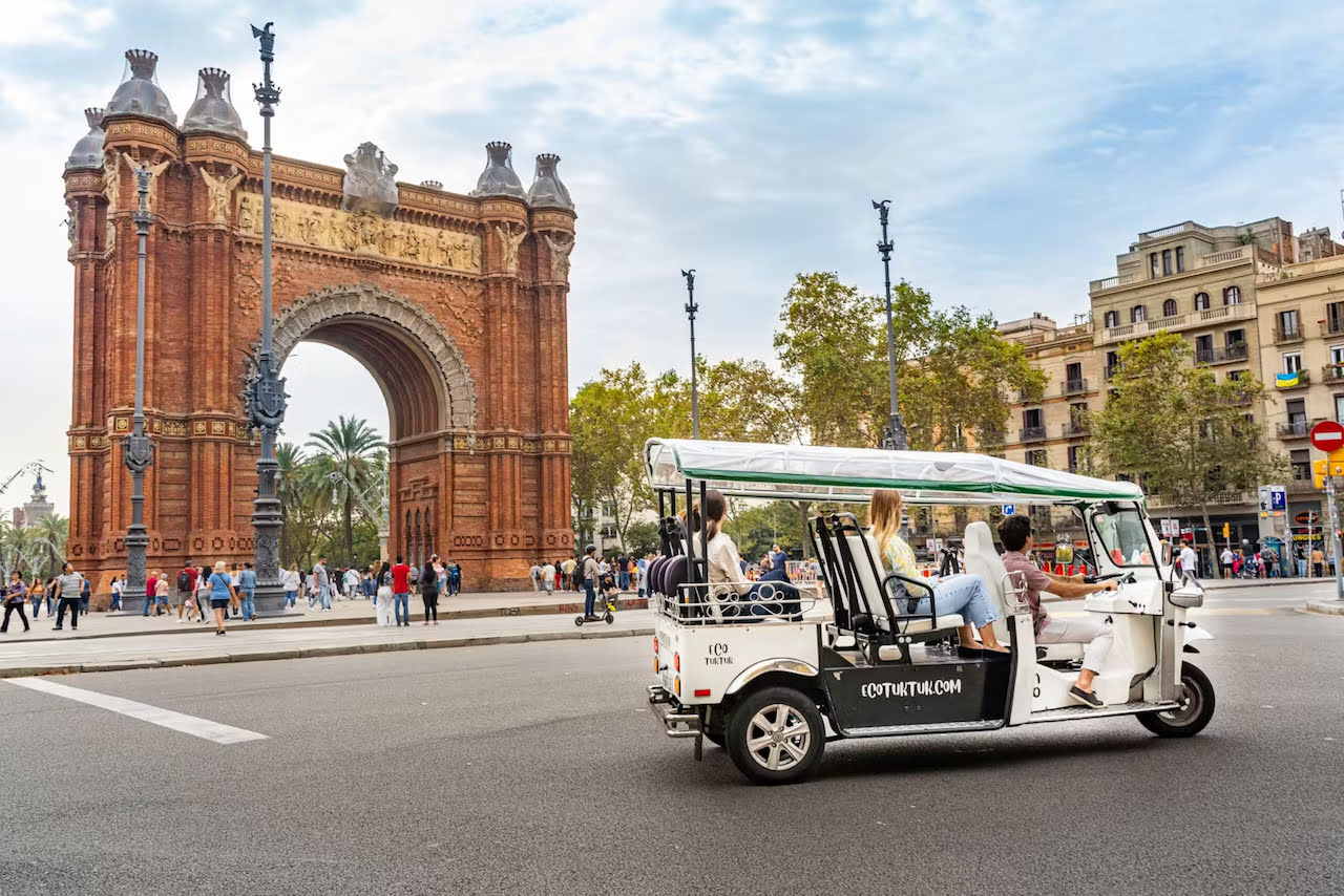 Electric tuk-tuk driving past the Arc de Triomf in Barcelona